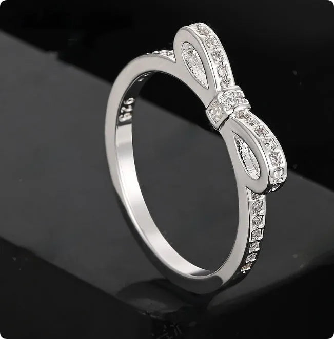 Silver couple's ring with a bow shape and sparkling zircon crystal rhinestones on a finger.