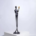 Black aluminium desktop sculpture of a woman reading, measuring 12cm wide by 51cm tall.