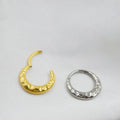Close-up of a concave-convex titanium nose ring in gold or silver finish, showing textured surface.
