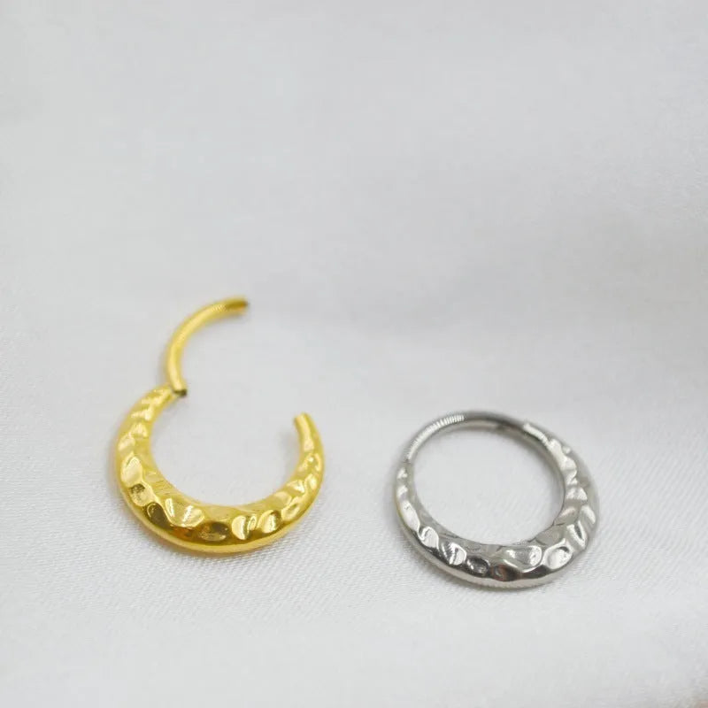 Close-up of a concave-convex titanium nose ring in gold or silver finish, showing textured surface.