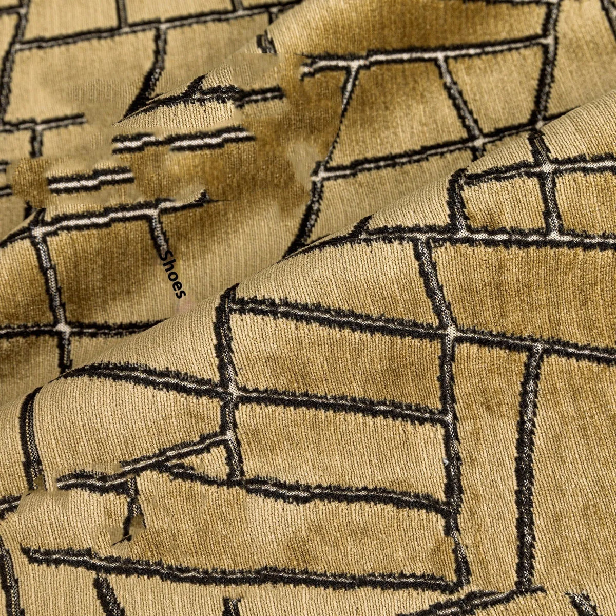 Gold geometric abstract pattern on a velvet square decorative cushion on a grey sofa.