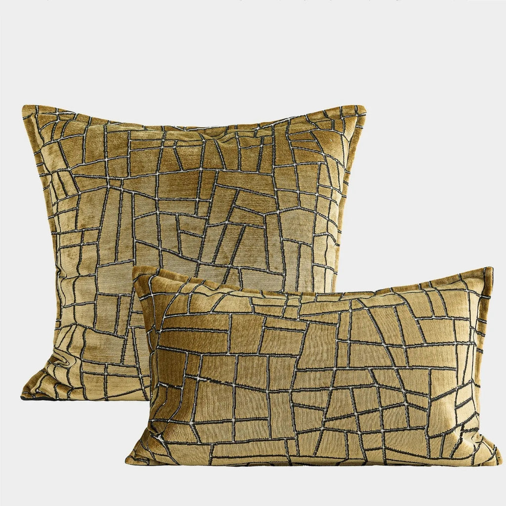Gold geometric abstract pattern on a velvet square decorative cushion on a grey sofa.