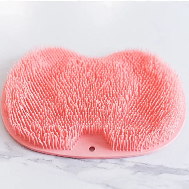 Orange silicone suction cup bath brush with bristles for back and foot massage on a bathroom floor.