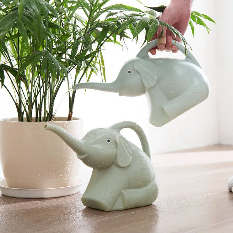 Pink baby elephant-shaped plastic watering can with a long spout on a wooden table.