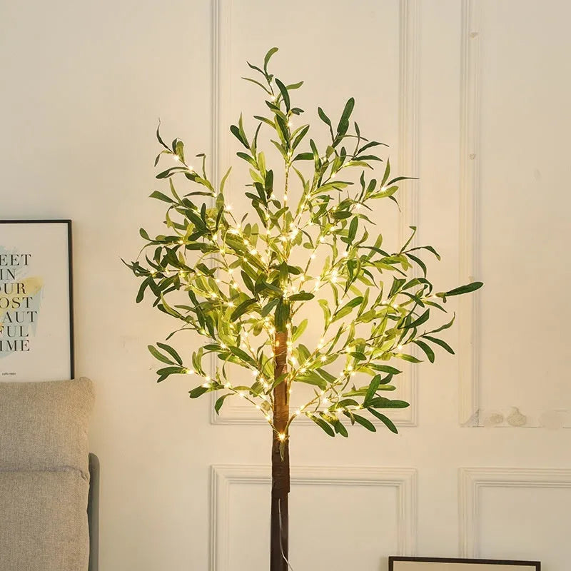 Tall artificial olive tree lamp with warm white LED lights illuminated in an outdoor courtyard setting.