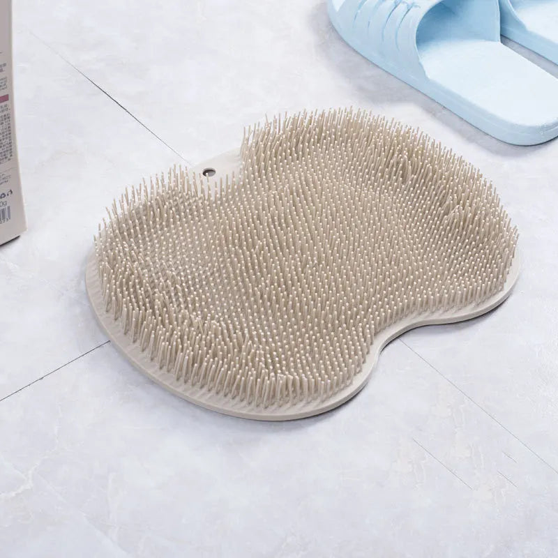 Orange silicone suction cup bath brush with bristles for back and foot massage on a bathroom floor.