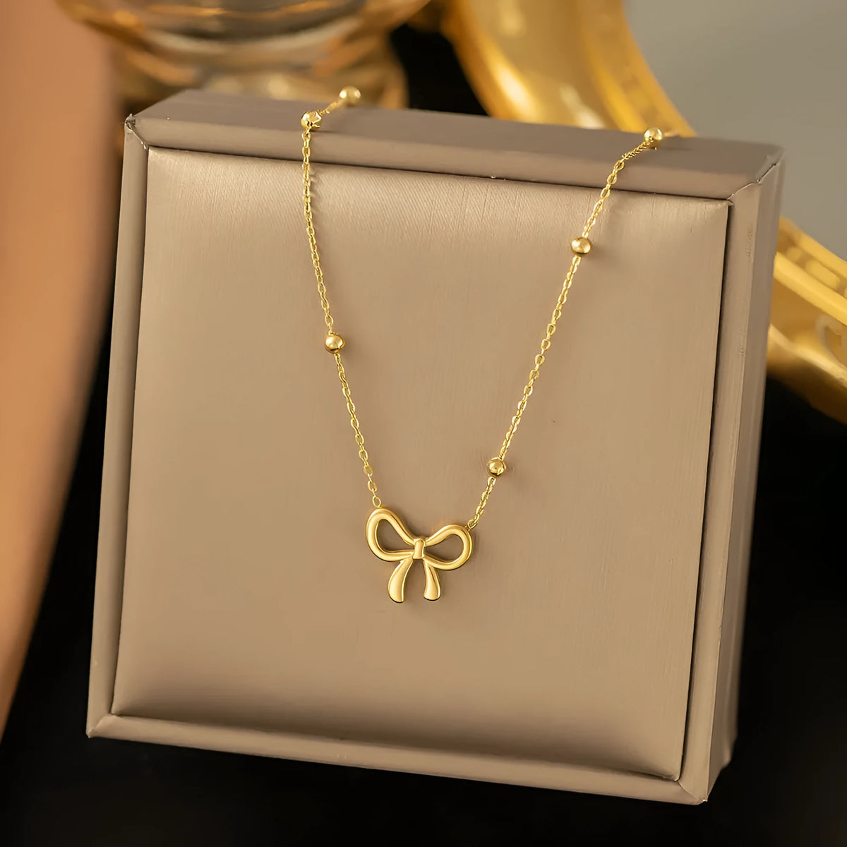 Gold electroplated titanium steel bow necklace with cross chain style on white background