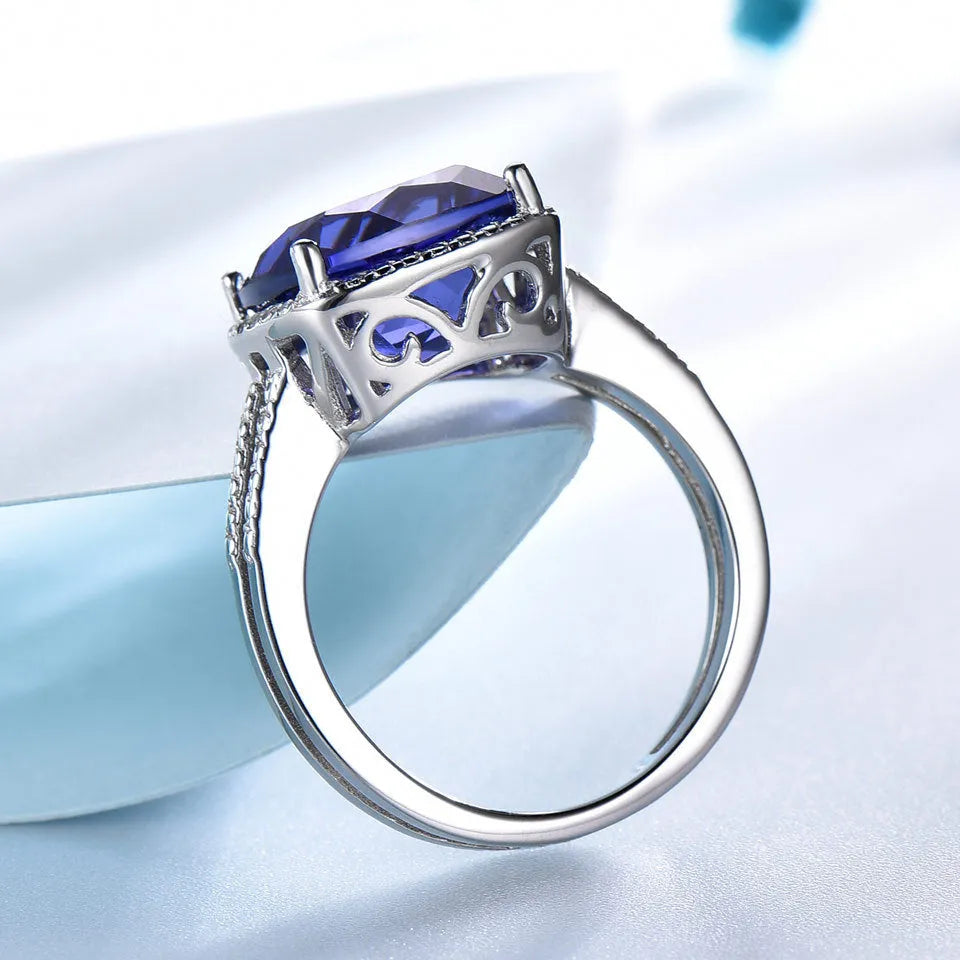 Blue tanzanite gemstone set in a sterling silver women's ring on a grey background.