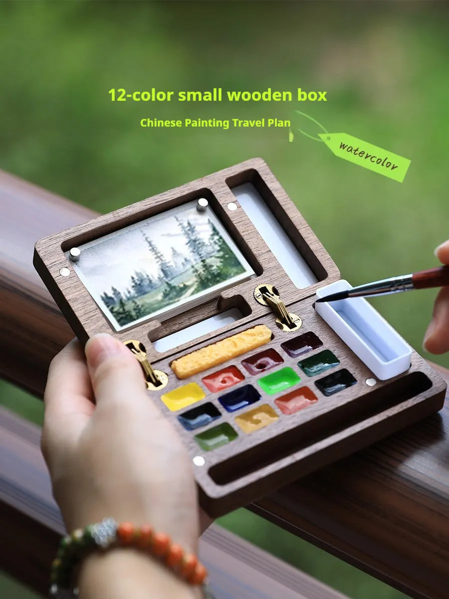 Miniature hinged wooden watercolour paint box open to show compartments for paints and brushes.