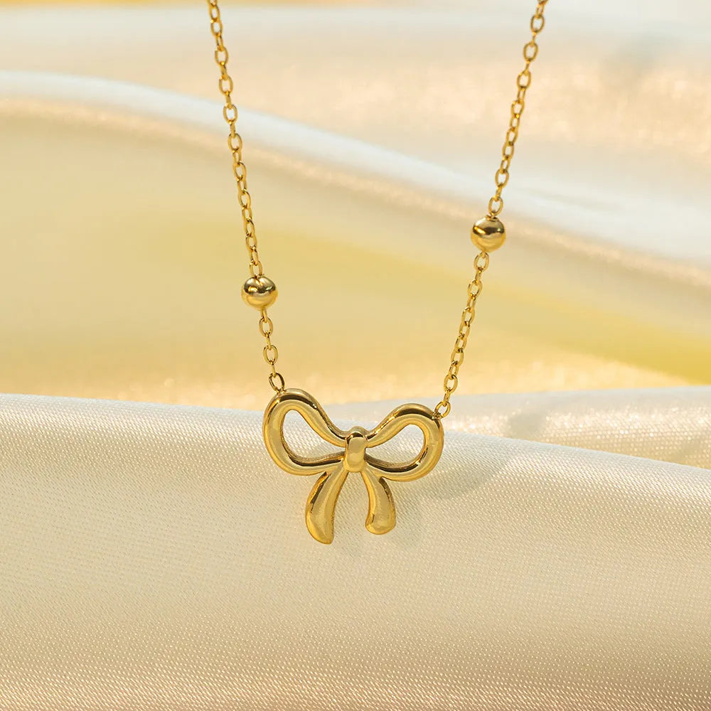Gold electroplated titanium steel bow necklace with cross chain style on white background