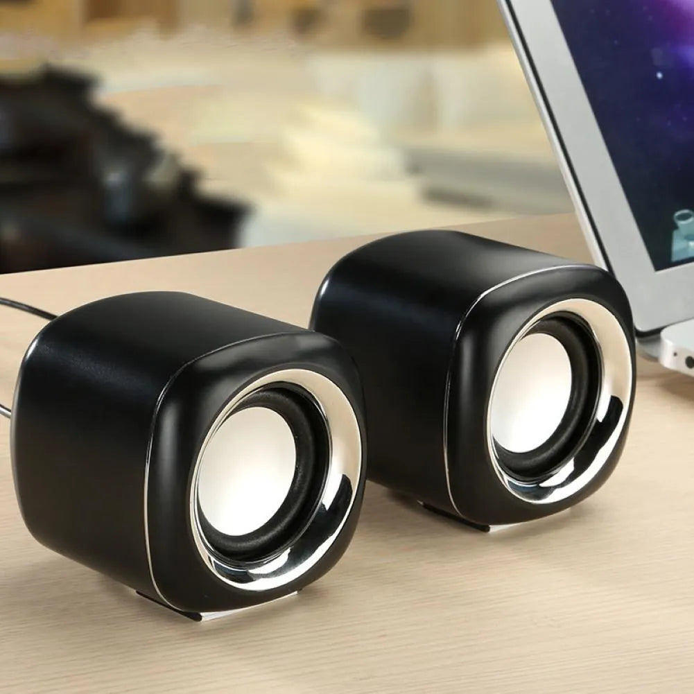 Compact black wired desktop computer speaker pair with 3.5mm plug next to a laptop.