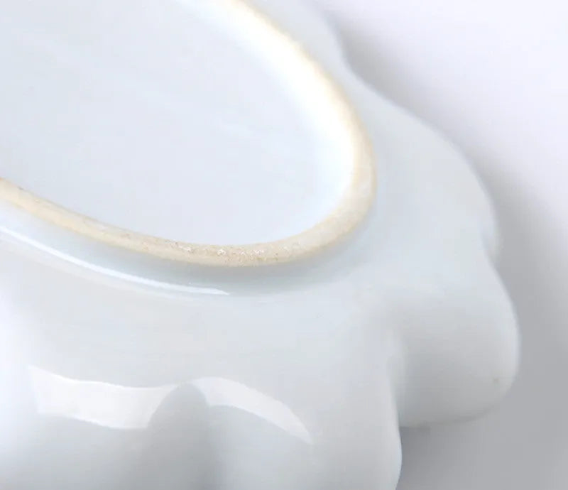 White ceramic plum blossom shaped artist's paint palette on a wooden table.