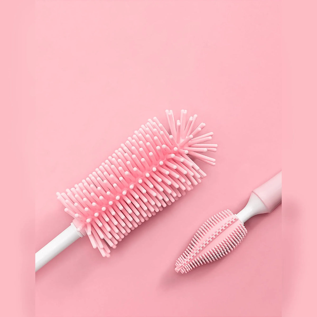 Three silicone baby bottle brushes on a counter, including a main brush and a narrow straw cleaning brush.