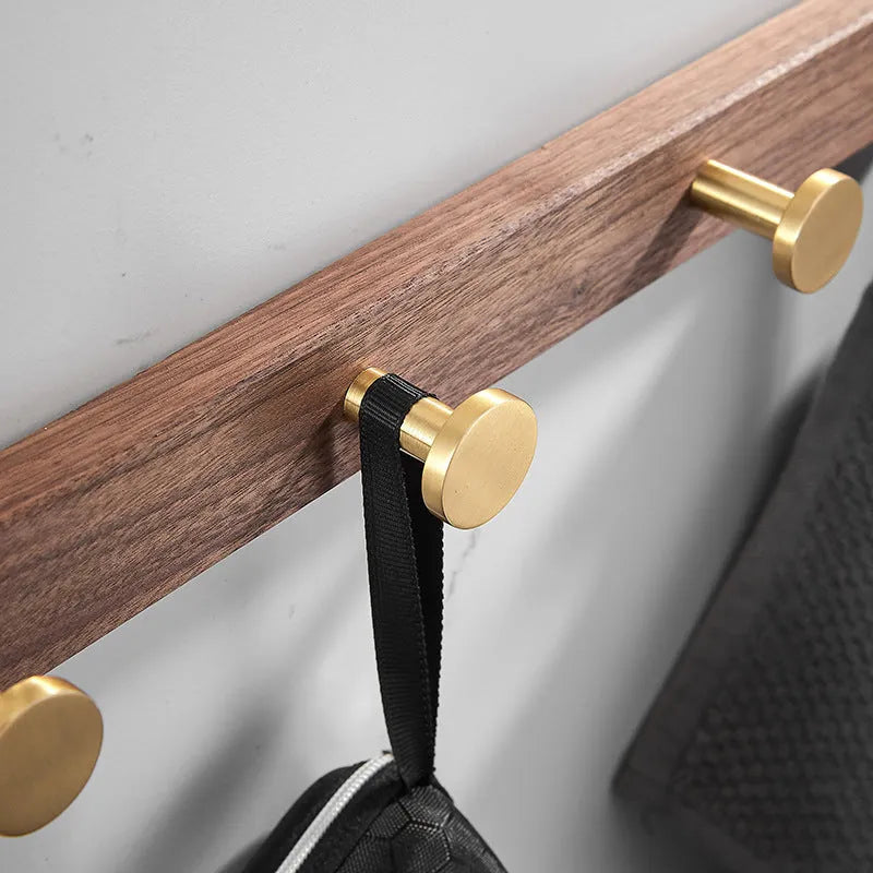 Set of black walnut aluminium clothes hooks with brass finish mounted on a perforated panel.