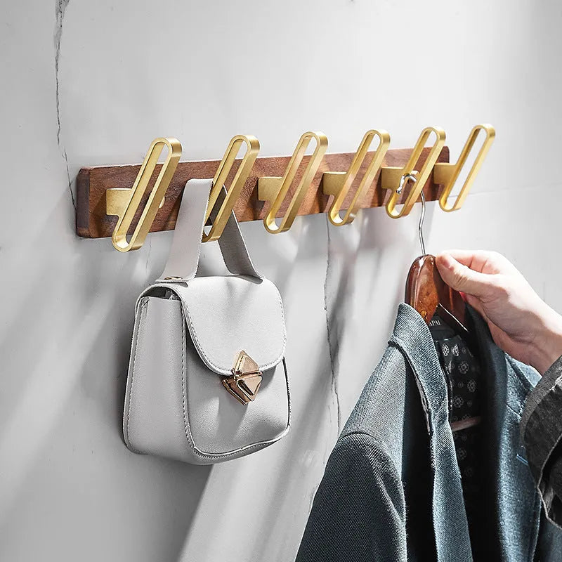 Set of black walnut aluminium clothes hooks with brass finish mounted on a perforated panel.