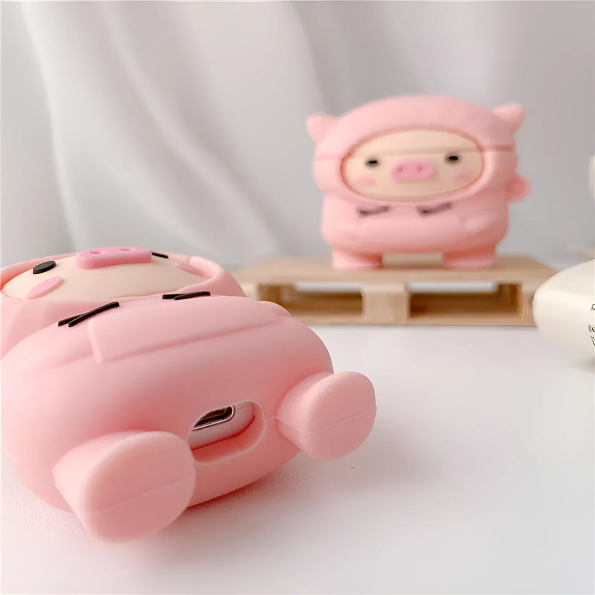 Pink silicone AirPods case with cartoon hoodie pig design, showing flip opening and attachment hook