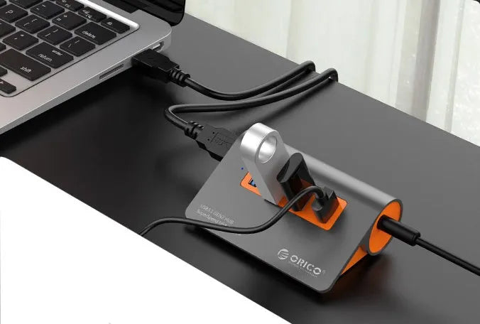 Dark grey aluminium USB hub with orange detailing showing four USB 3.1 ports and detachable cable