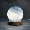 Nordic style USB table lamp with a glass shade in one of seven colour options on a bedside table.