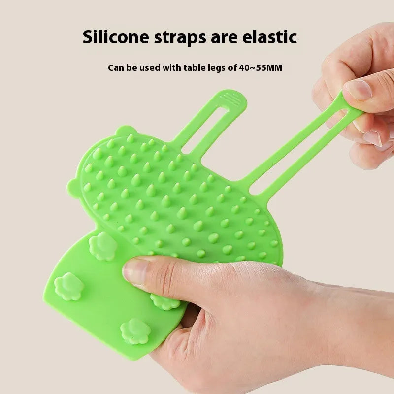 Silicone cat grooming comb with adjustable strap attached to table leg for hair removal and scratching relief