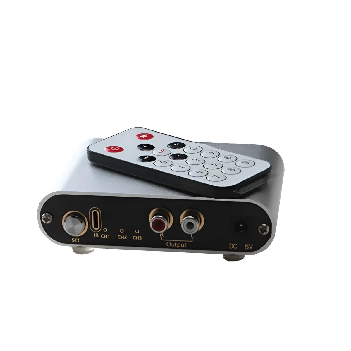Silver aluminium audio source selector switch box with remote control on a dark surface.