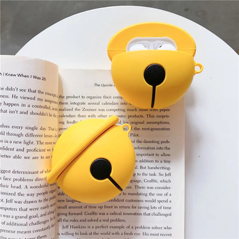 Yellow silicone AirPods case with attached bell charm showing charging port and LED cutouts