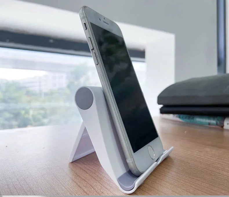 Black folding mobile phone stand holding a smartphone at an angle on a wooden table