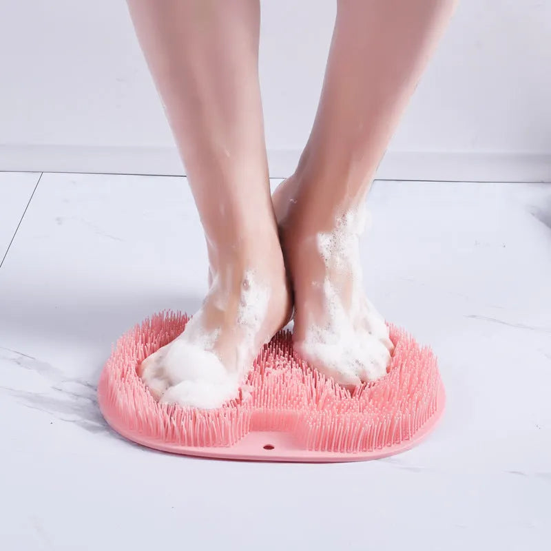 Orange silicone suction cup bath brush with bristles for back and foot massage on a bathroom floor.