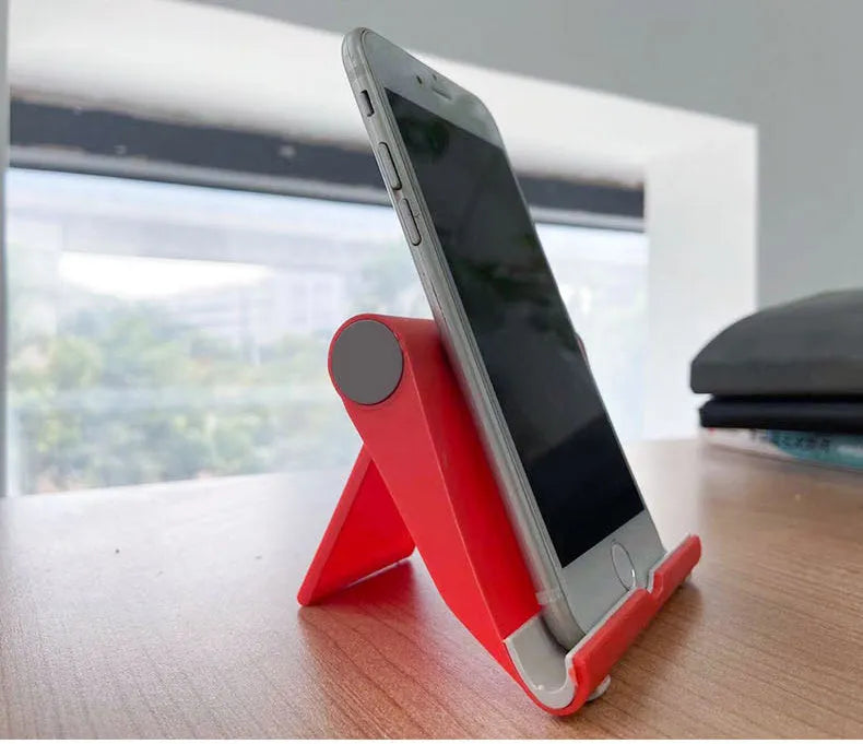 Black folding mobile phone stand holding a smartphone at an angle on a wooden table