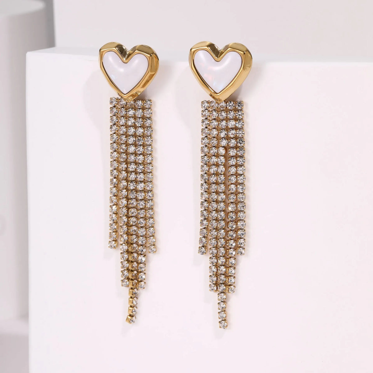 Women's gold heart and star shaped earrings with a diamond tassel detail on a white background.