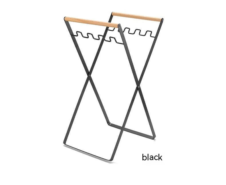 Black folding iron trash rack with wooden handle holding a bin bag outdoors.