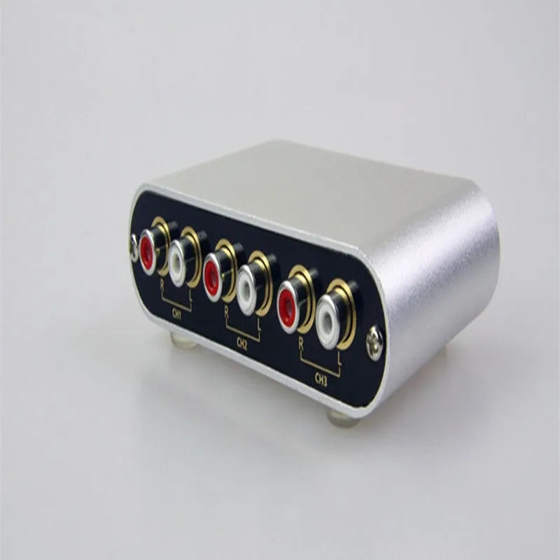 Silver aluminium audio source selector switch box with remote control on a dark surface.