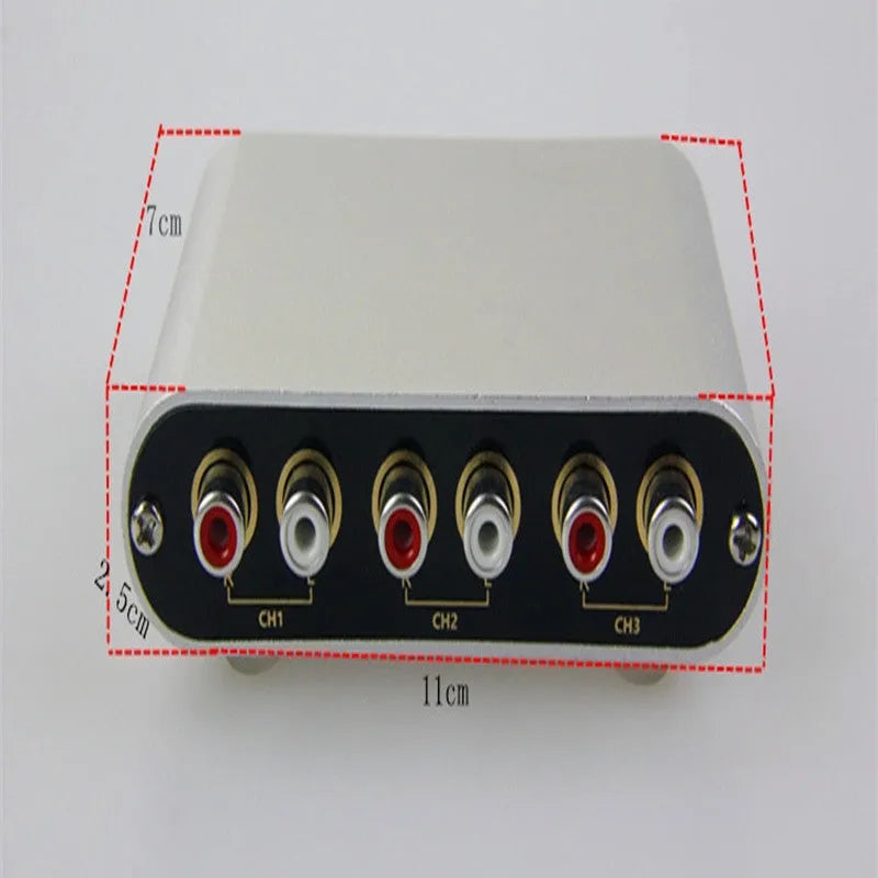 Silver aluminium audio source selector switch box with remote control on a dark surface.