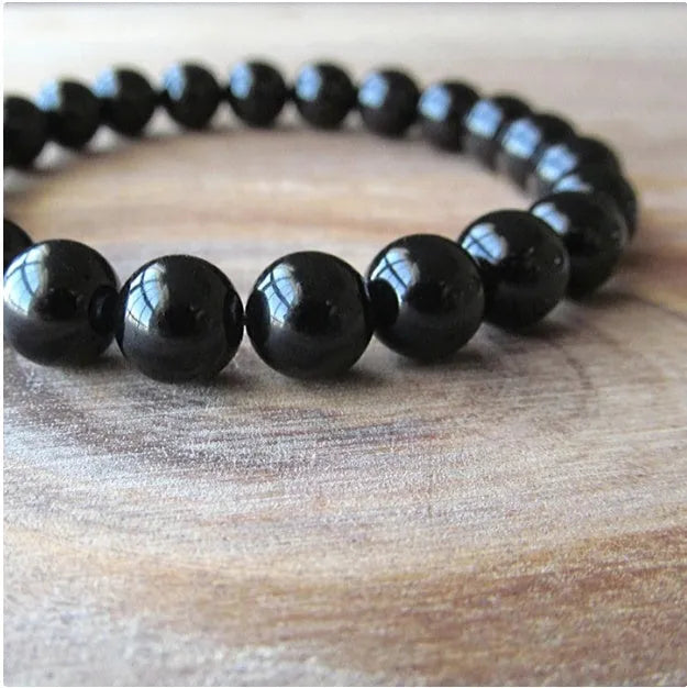 Geometric black onyx bracelet with 8mm beads on a black elastic cord, laid flat.