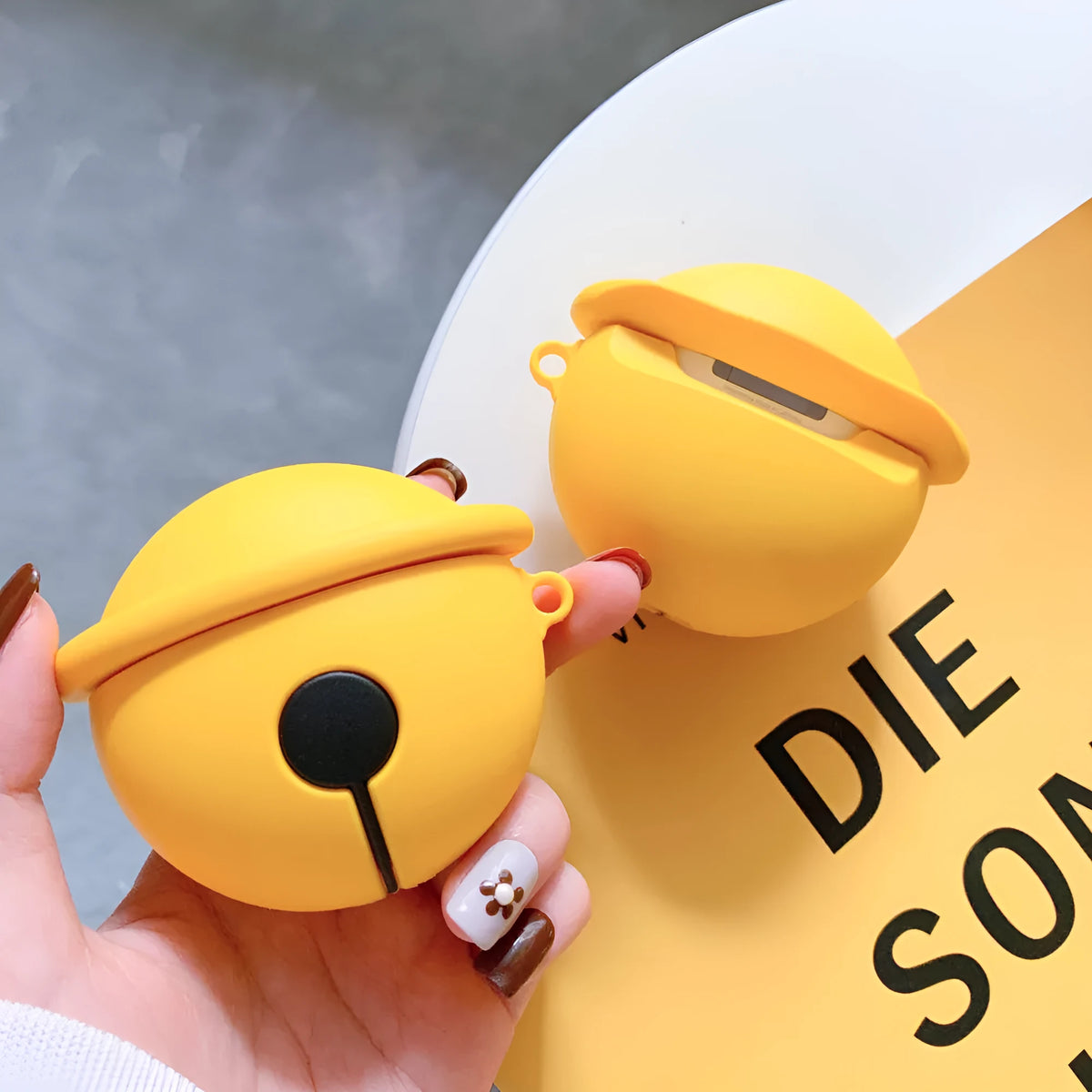 Yellow silicone AirPods case with attached bell charm showing charging port and LED cutouts