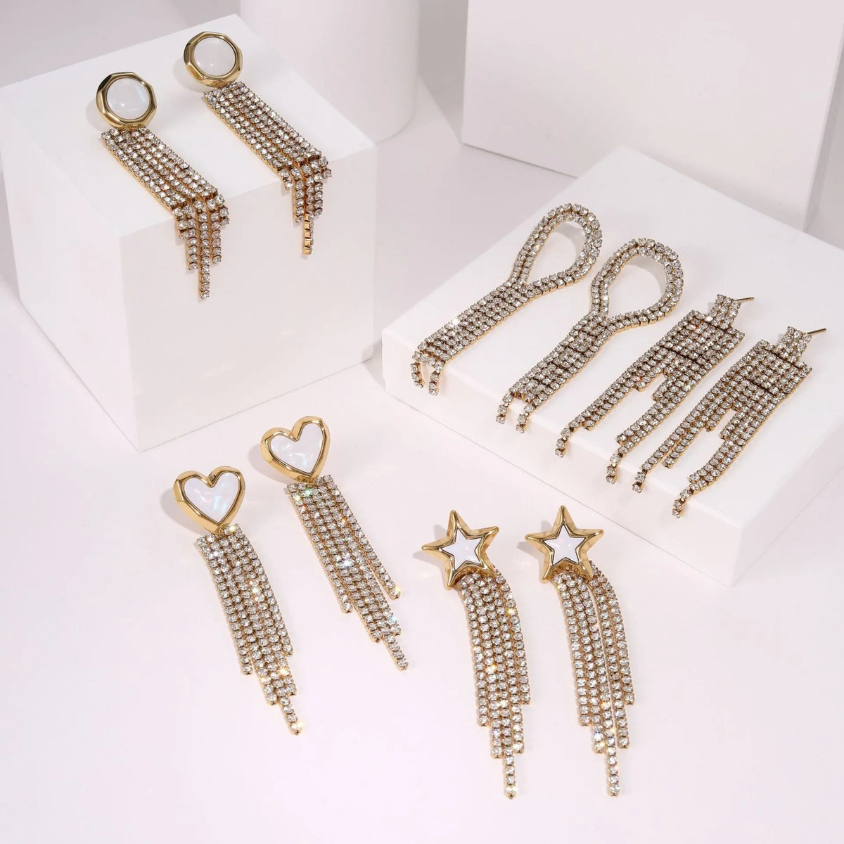 Women's gold heart and star shaped earrings with a diamond tassel detail on a white background.