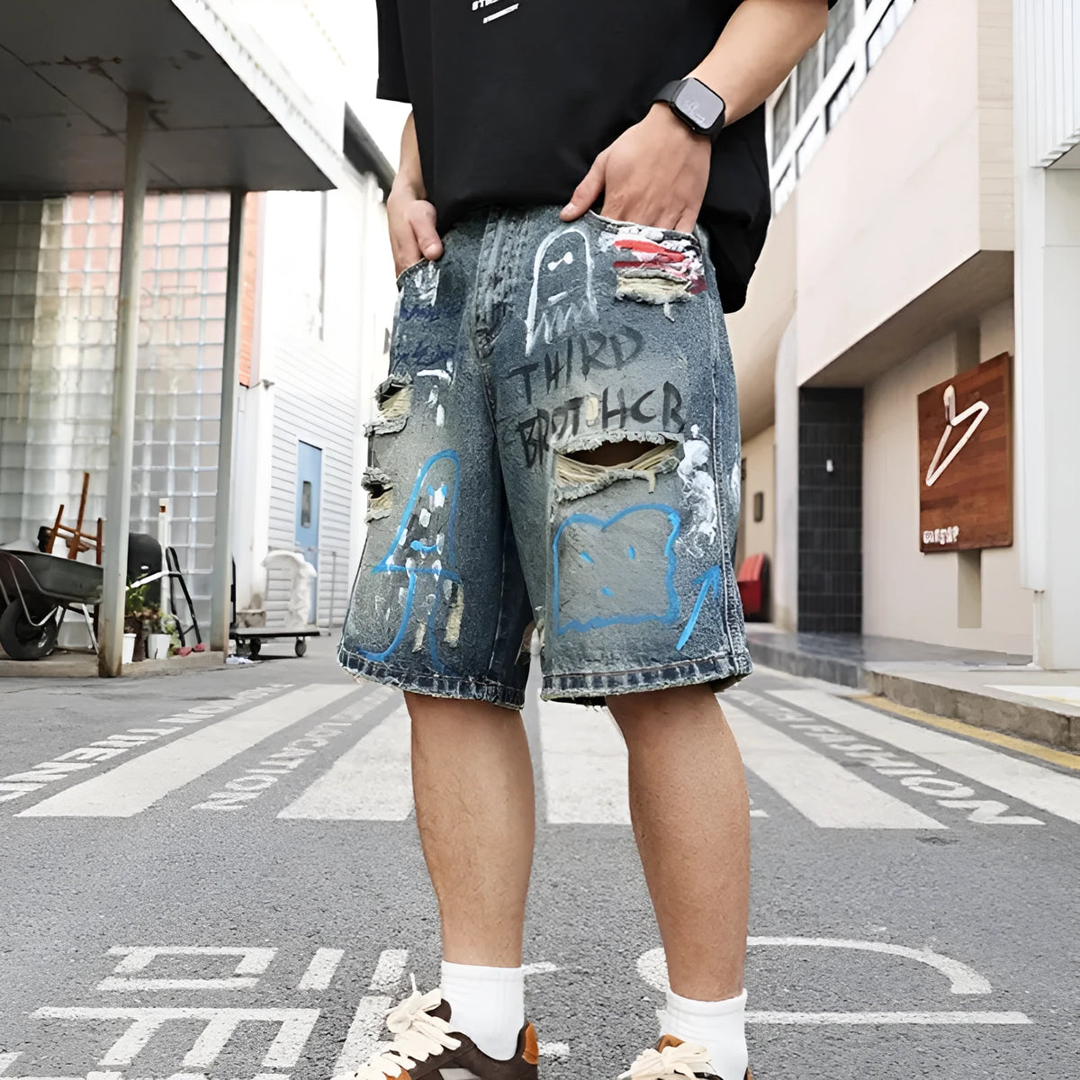 Blue men's denim shorts with ripped knees and graffiti-style print, featuring a straight leg and zipper fly.