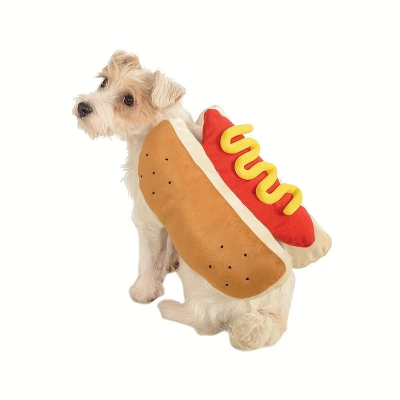 Small dog wearing a red and brown plush hot dog costume with bun and sausage design.