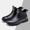 Short tube black PVC rain boots with round toe and flat heel on a non-slip plastic sole.