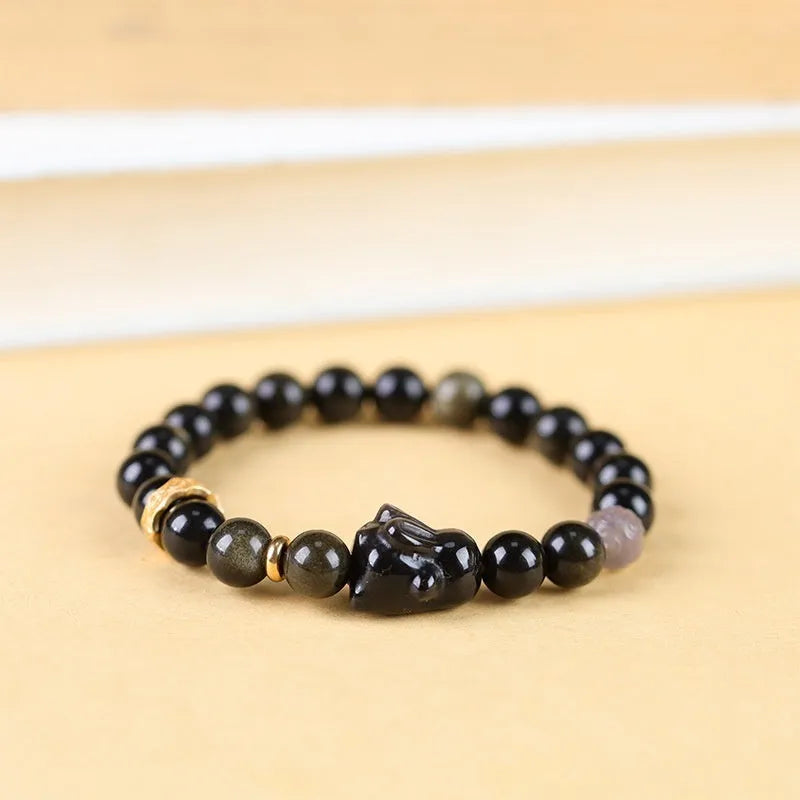 Close-up of a handmade lying rabbit obsidian bracelet in brass with grey agate beads.