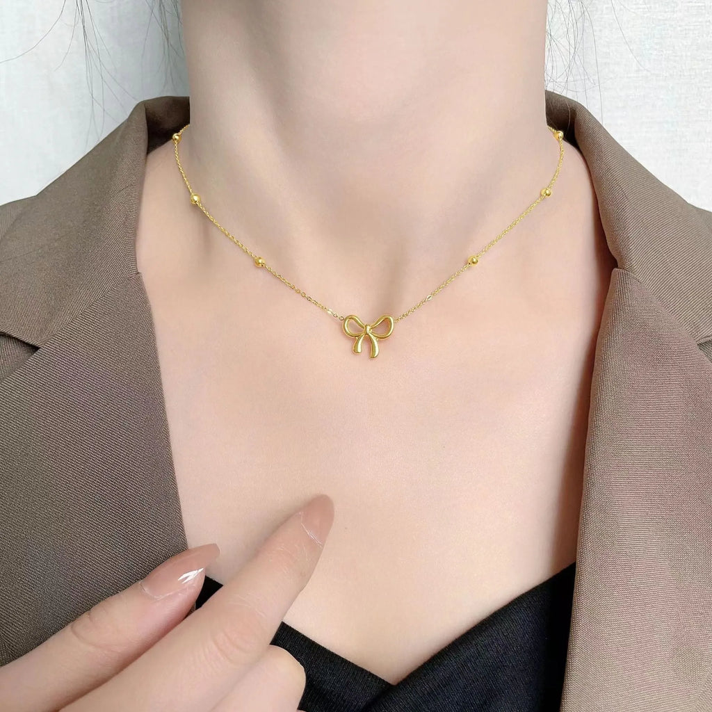 Gold electroplated titanium steel bow necklace with cross chain style on white background