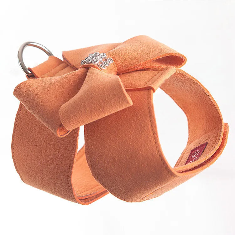 A pink microfiber puppy chest strap harness with a large central bowknot, showing adjustable buckles.