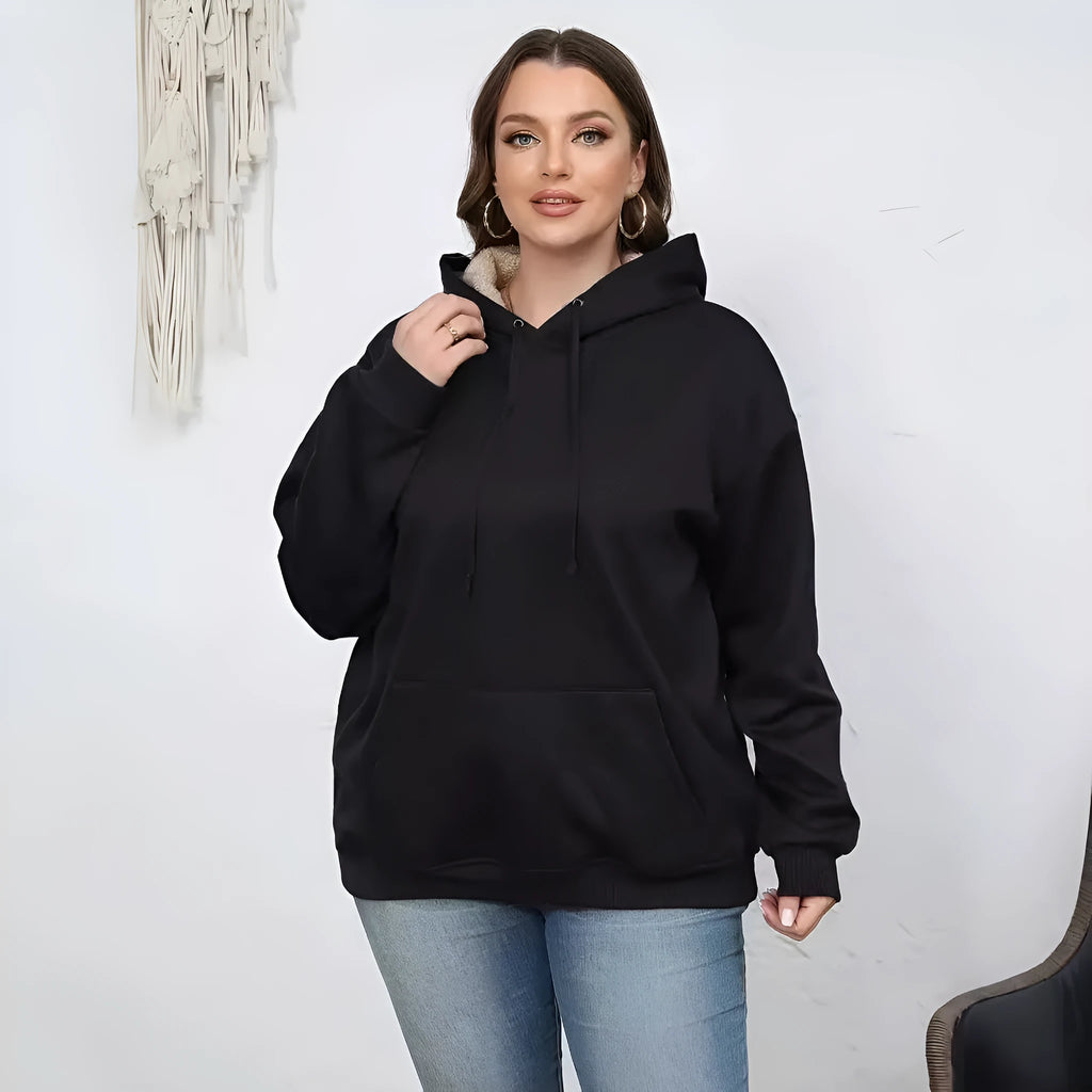 Woman wearing a loose grey hooded sweater with a front kangaroo pocket.