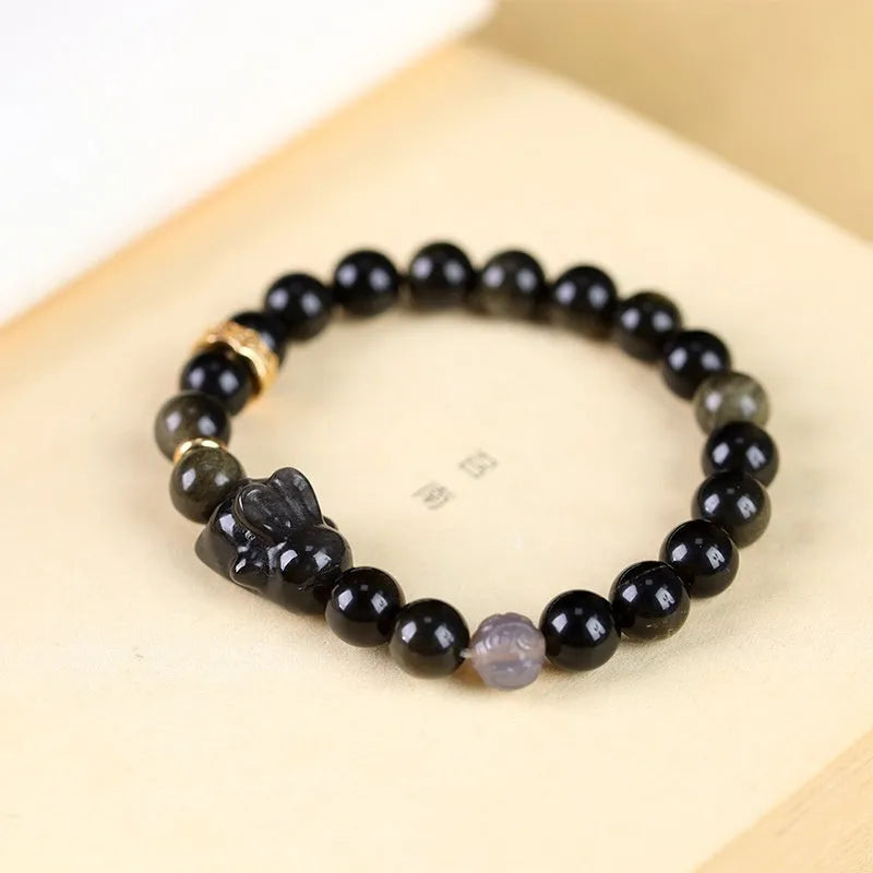 Close-up of a handmade lying rabbit obsidian bracelet in brass with grey agate beads.
