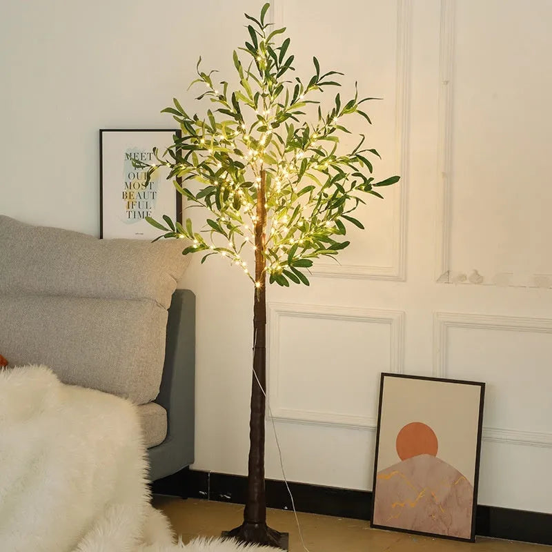 Tall artificial olive tree lamp with warm white LED lights illuminated in an outdoor courtyard setting.