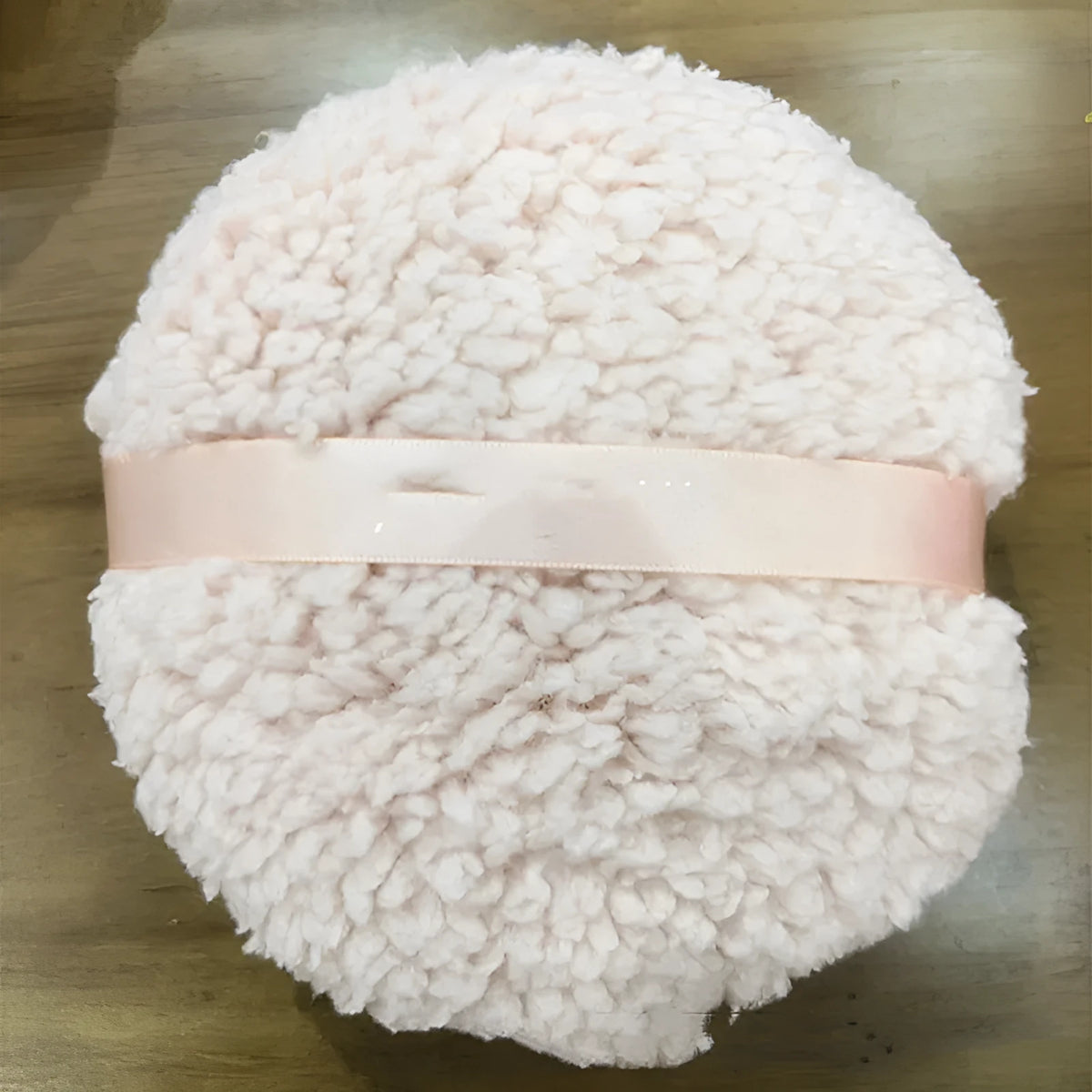 Oversized rectangular plush powder puff in skin colour on a pink background
