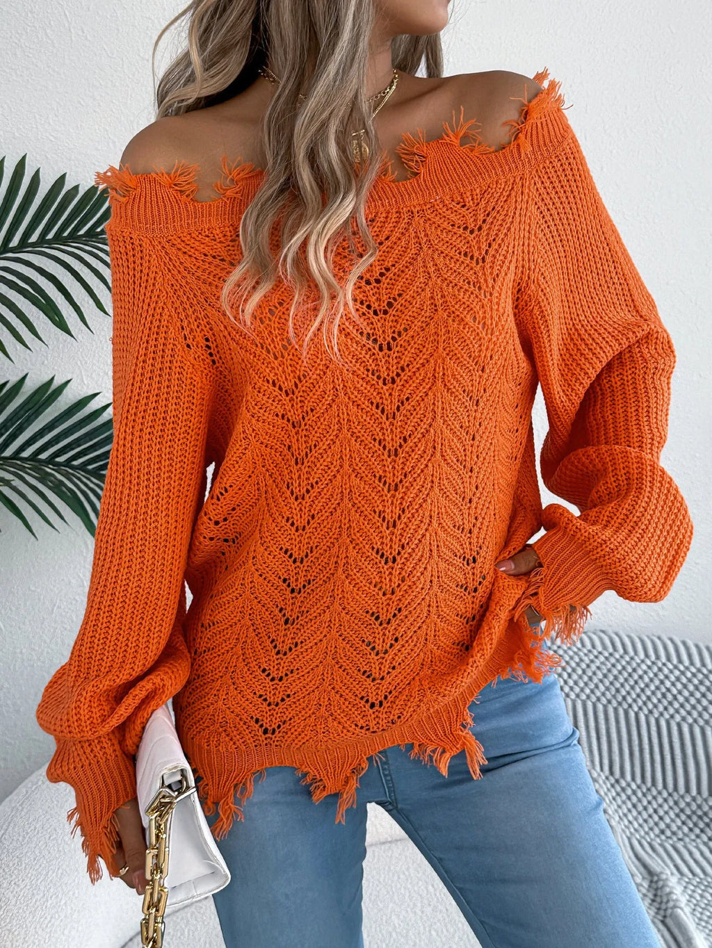 White hollow-out cut off-the-shoulder long sleeve pullover sweater on a hanger showing acrylic knit fabric detail.