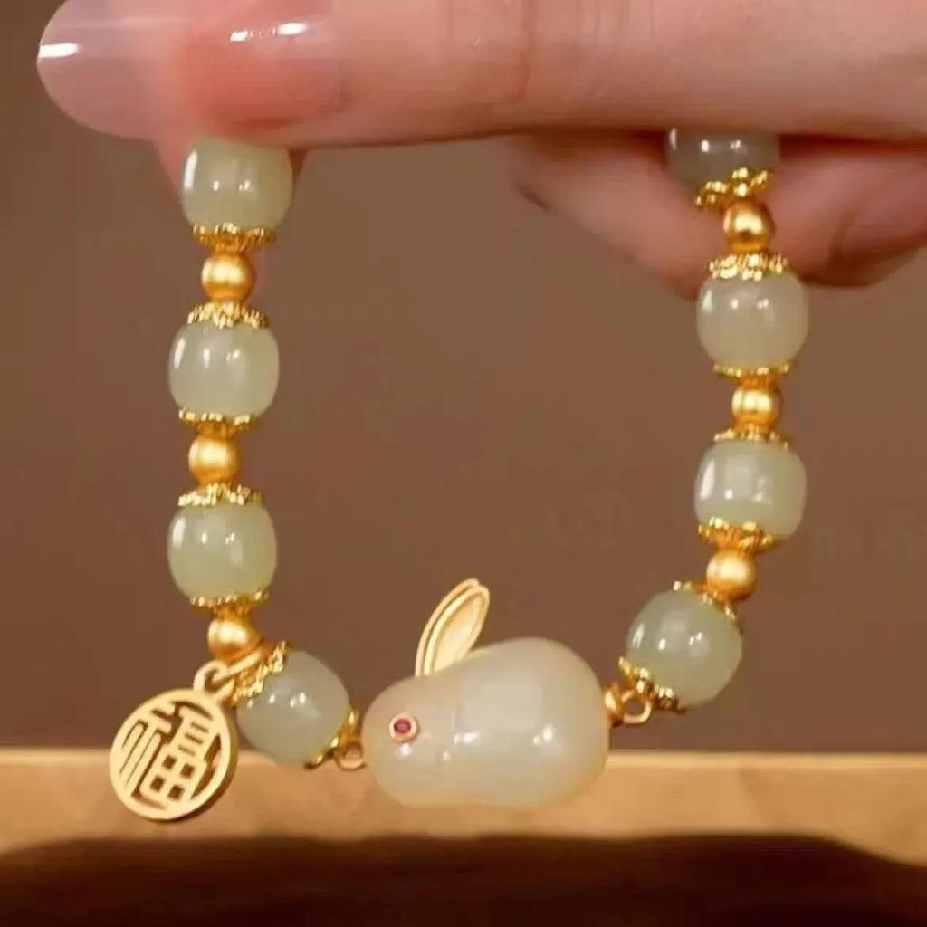 Close-up of a black women's bracelet with a green jade fu character charm and a metal hare pendant.