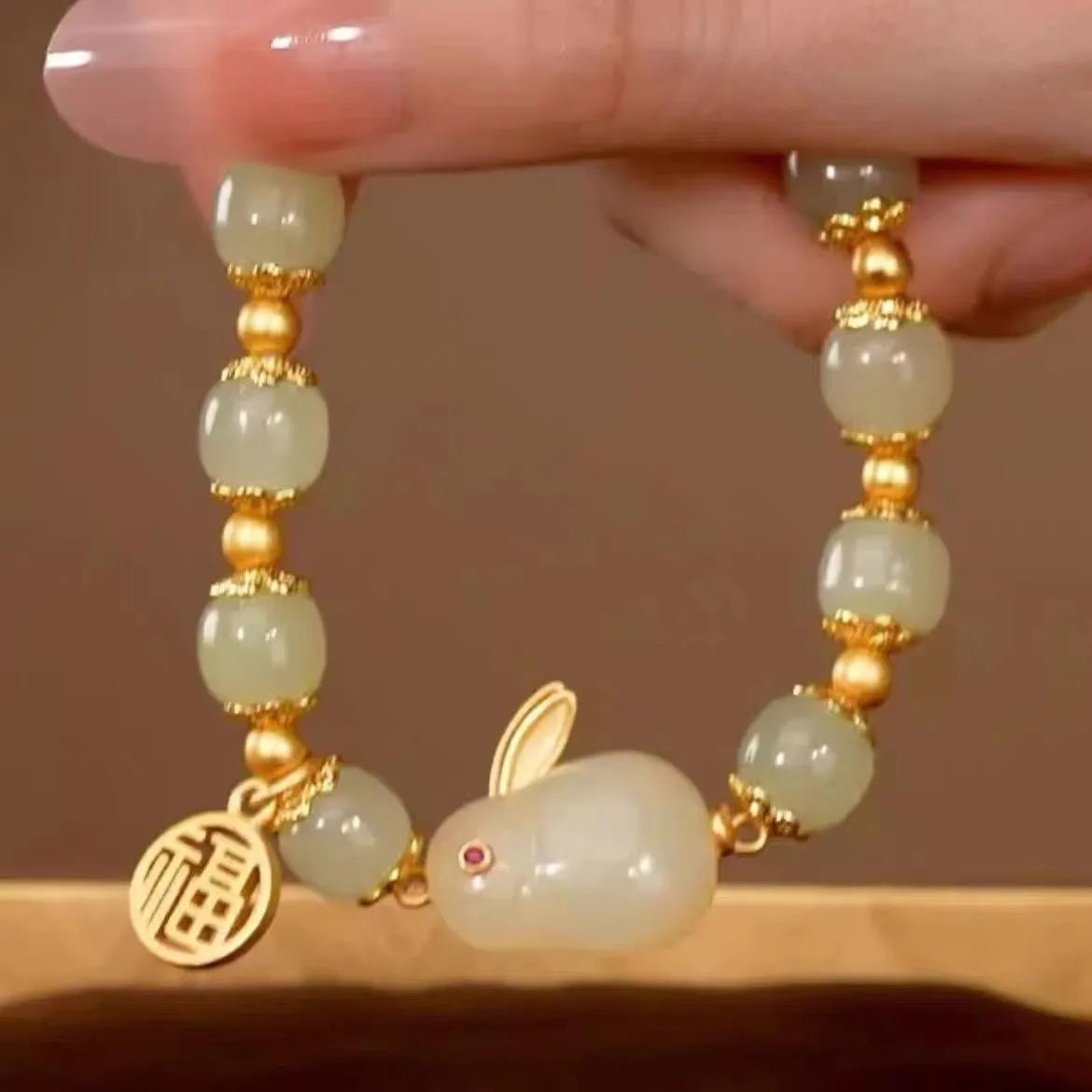 Close-up of a black women's bracelet with a green jade fu character charm and a metal hare pendant.