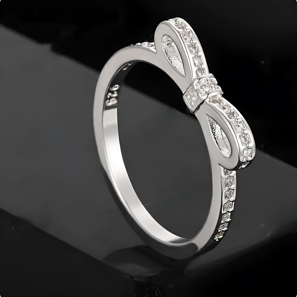 Silver couple's ring with a bow shape and sparkling zircon crystal rhinestones on a finger.