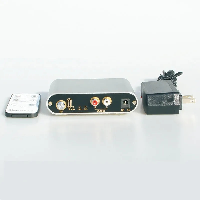 Silver aluminium audio source selector switch box with remote control on a dark surface.